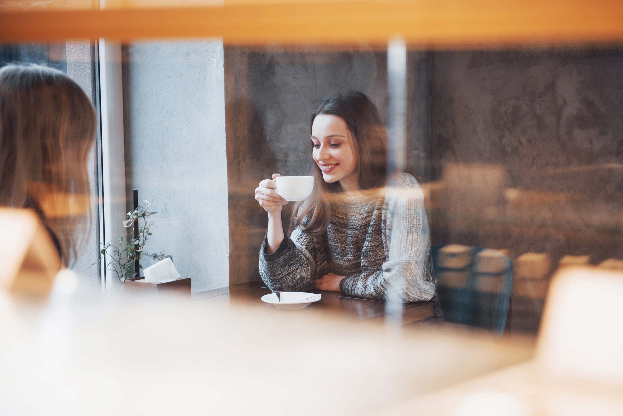 Two friends enjoying coffee together in a coffee shop as they sit at a table chatting